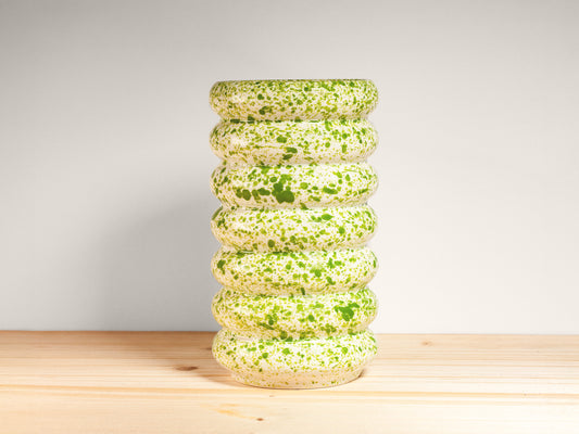 White and green ceramic vase on a wooden surface with a light gray background