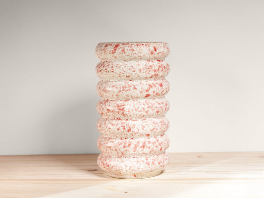 Speckled ceramic vase on a wooden surface with a light gray background