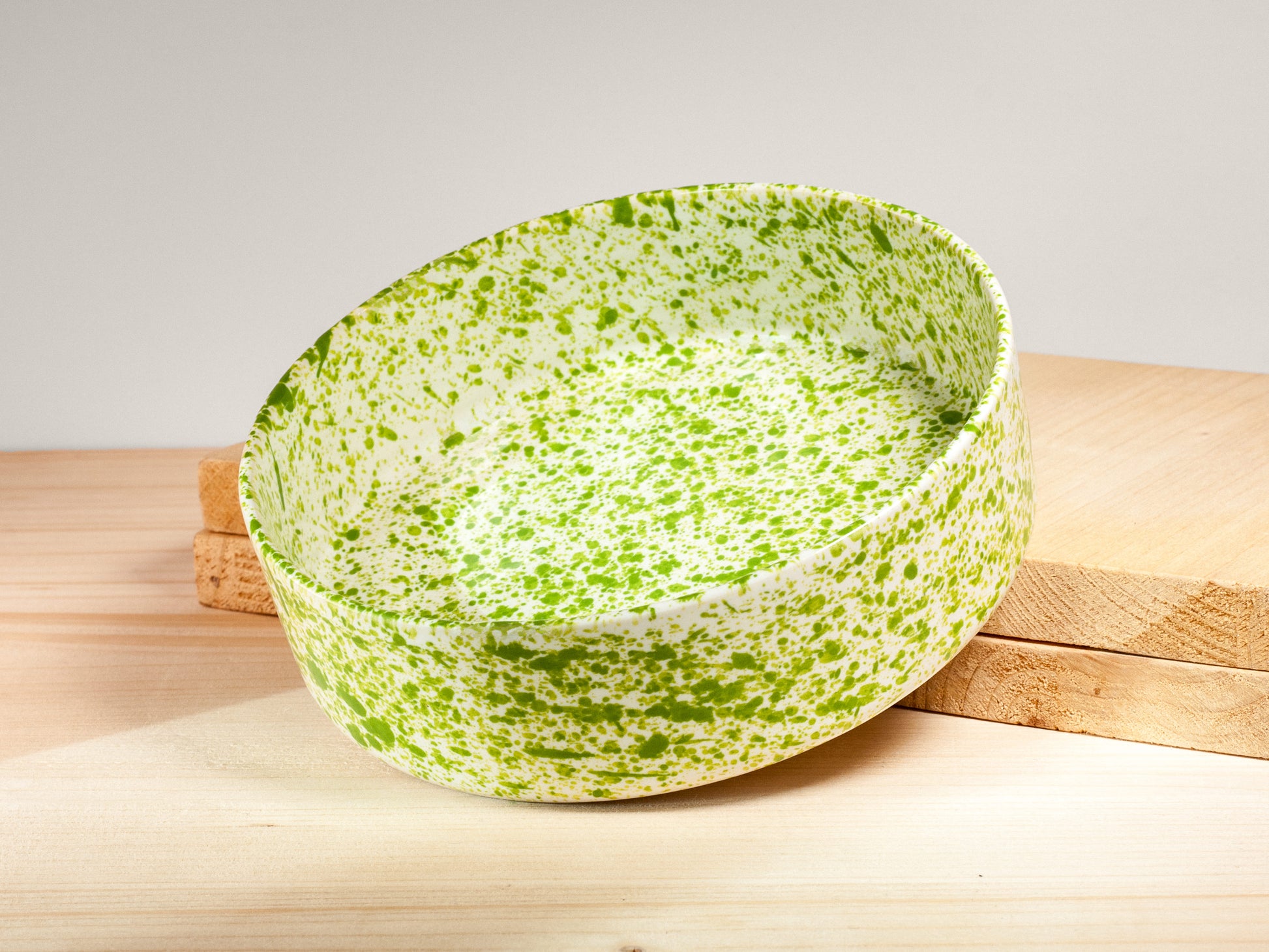 Green and white speckled bowl on a wooden surface with a light gray background