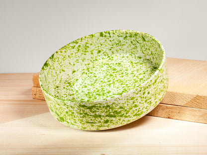 Green and white speckled bowl on a wooden surface with a light gray background