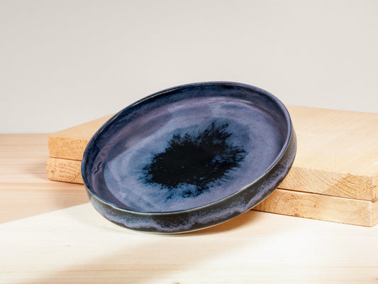 Blue ceramic plate with a black center on a wooden block against a light background