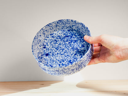 Hand holding a blue speckled ceramic bowl against a neutral background