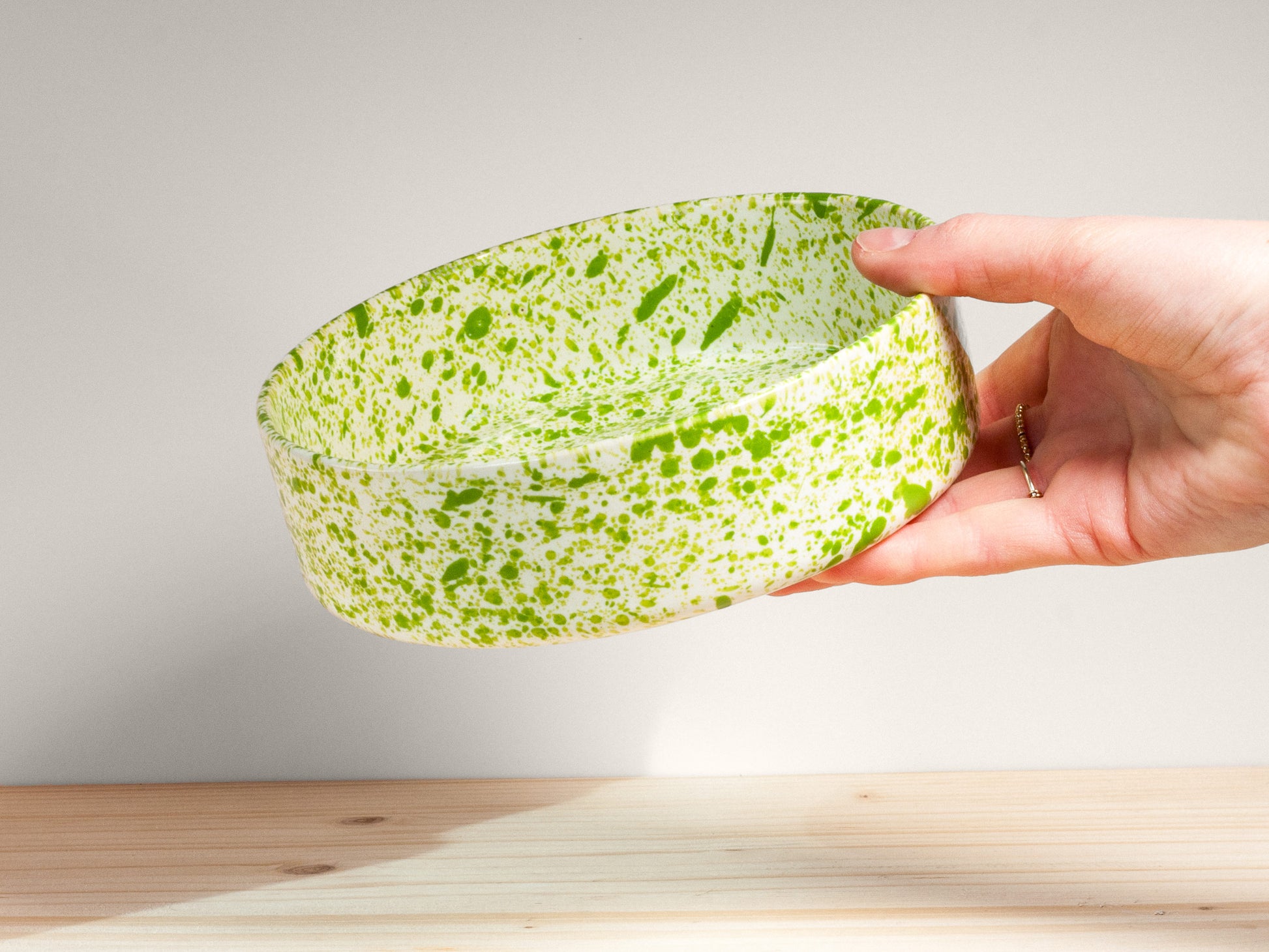 Hand holding a green and white patterned bowl against a light background