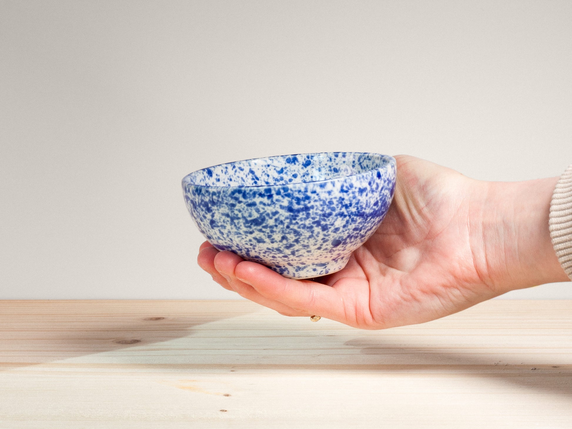 Hand holding a blue and white speckled ceramic bowl on a light wooden surface.