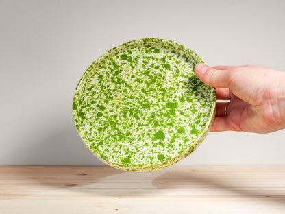 Hand holding a green ceramic plate with white speckles on a wooden surface.