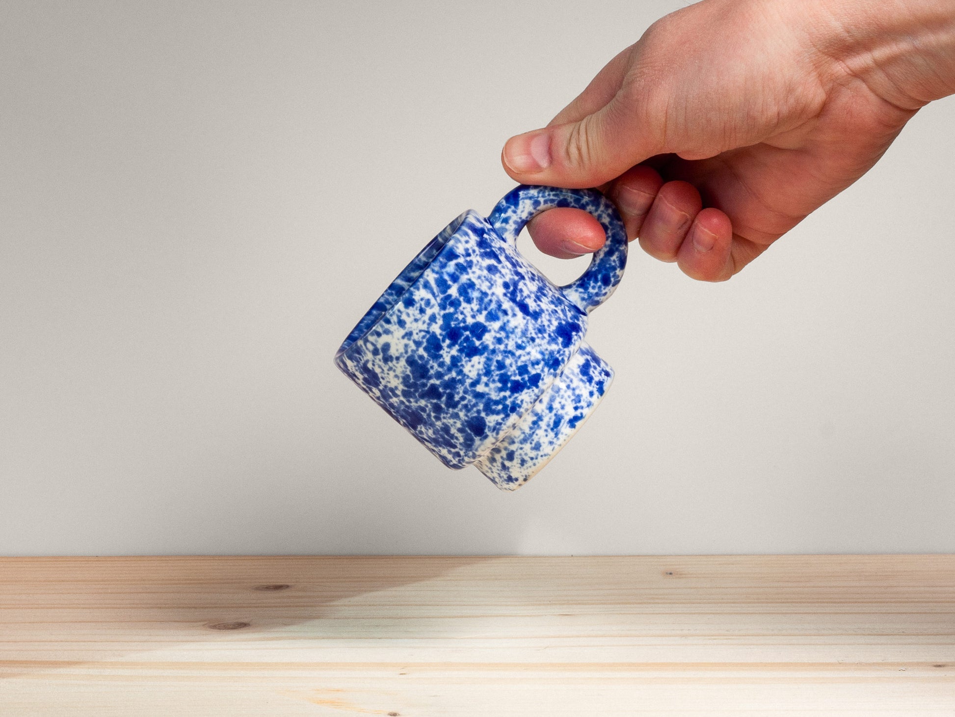 Hand holding a small blue and white ceramic mug against a plain background