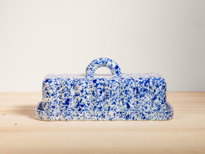 Blue and white speckled butter dish on a wooden surface with a light gray background