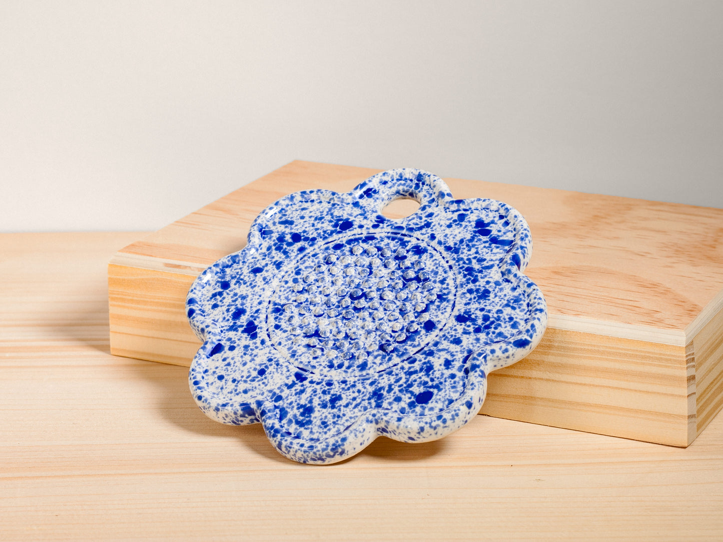 Blue and white ceramic flower-shaped garlic grater on a wooden surface