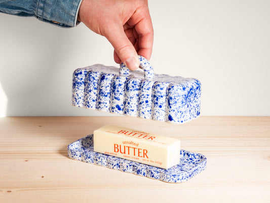 Butter dish with a stick of butter on a wooden surface, held by a hand.