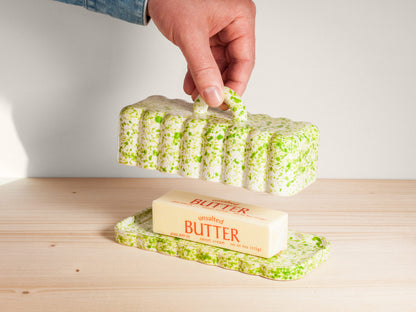 Butter dish with a block of butter on a wooden surface, hand holding the lid.
