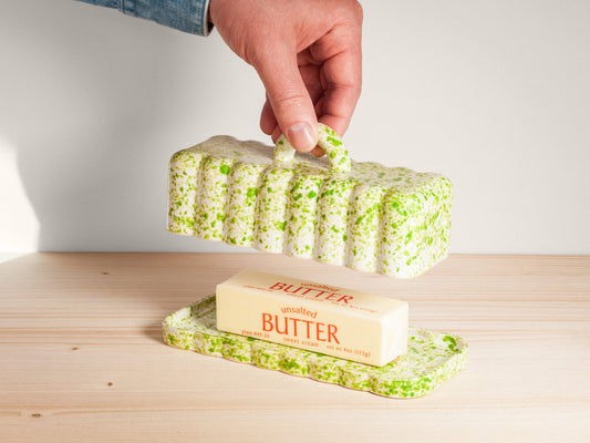 Butter dish with a block of butter on a wooden surface, hand holding the lid.