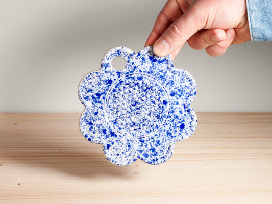 Hand holding a blue speckled ceramic flower-shaped garlic grater on a wooden surface with a neutral background