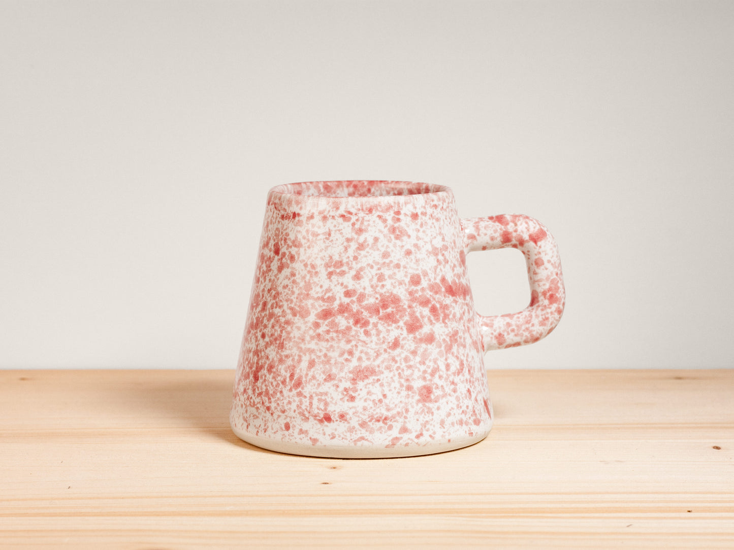 Pink and white ceramic mug on wooden surface with plain background