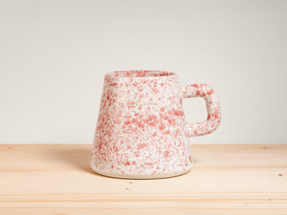 Pink and white ceramic mug on wooden surface with plain background