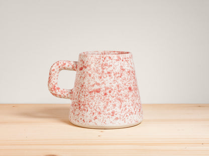 Pink and white ceramic mug on wooden surface with plain background
