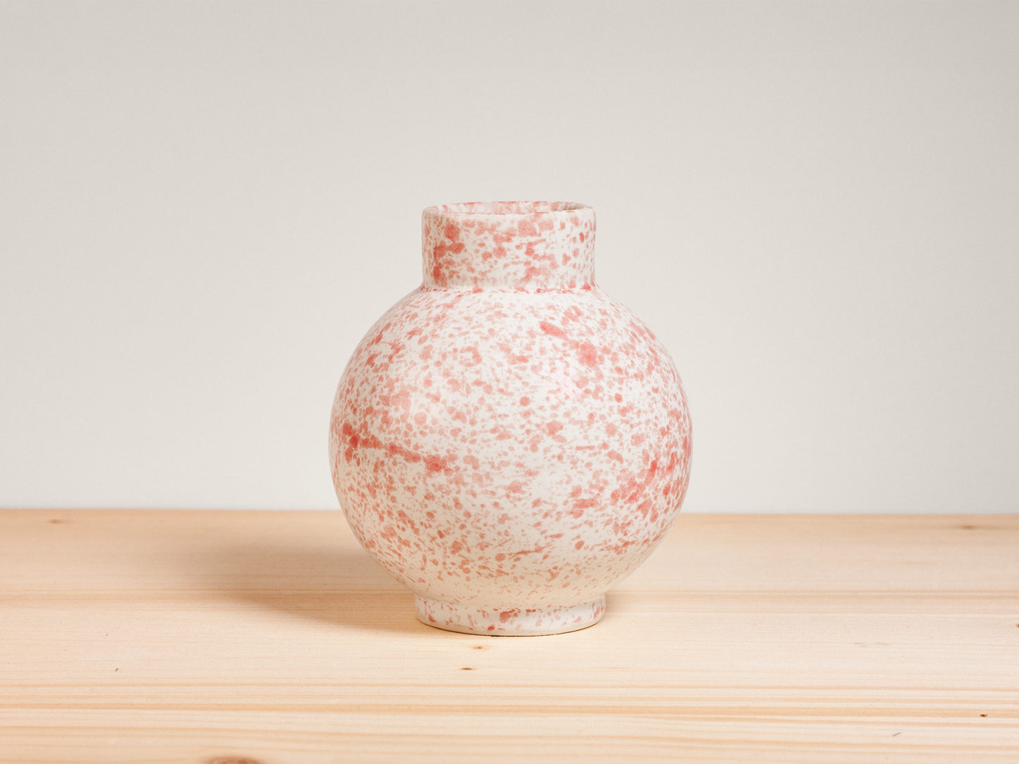 Pink and white ceramic vase on a wooden surface with a plain background