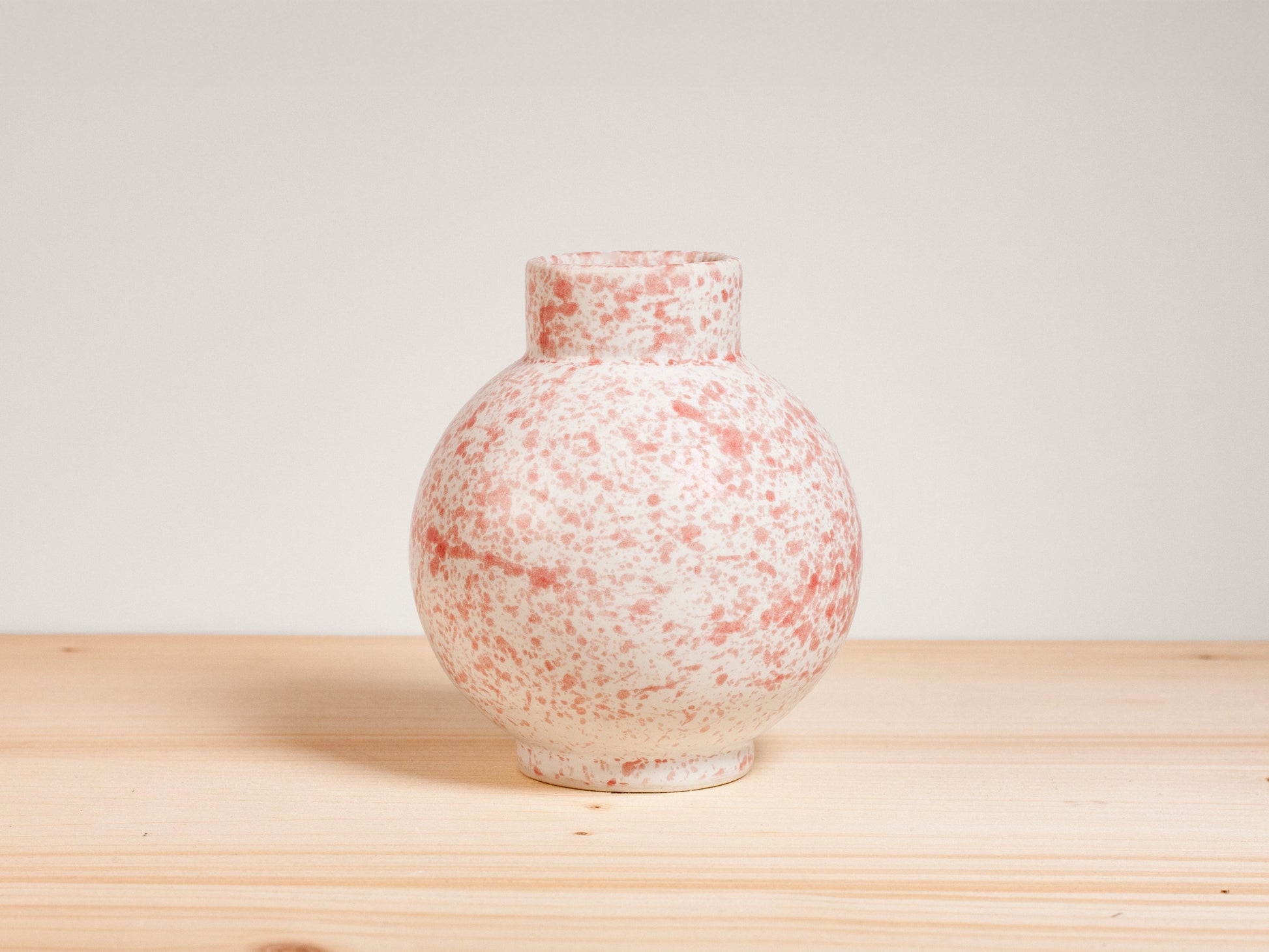 Pink and white ceramic vase on a wooden surface with a plain background