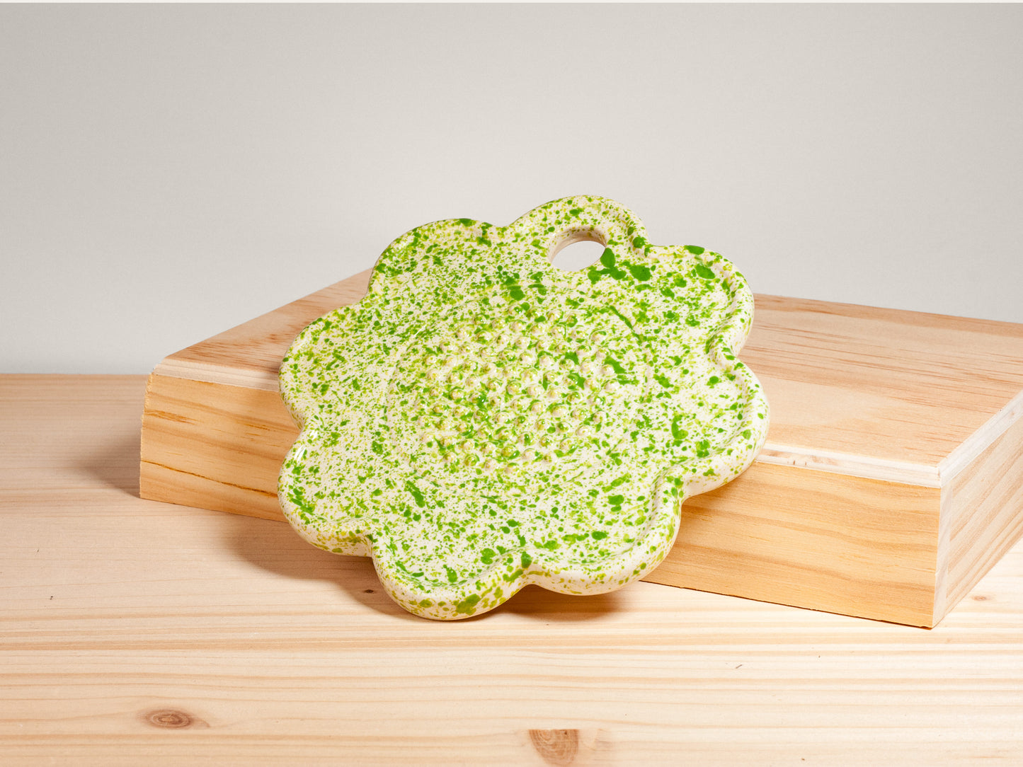 Green and white flower-shaped ceramic garlic grater on wooden surface