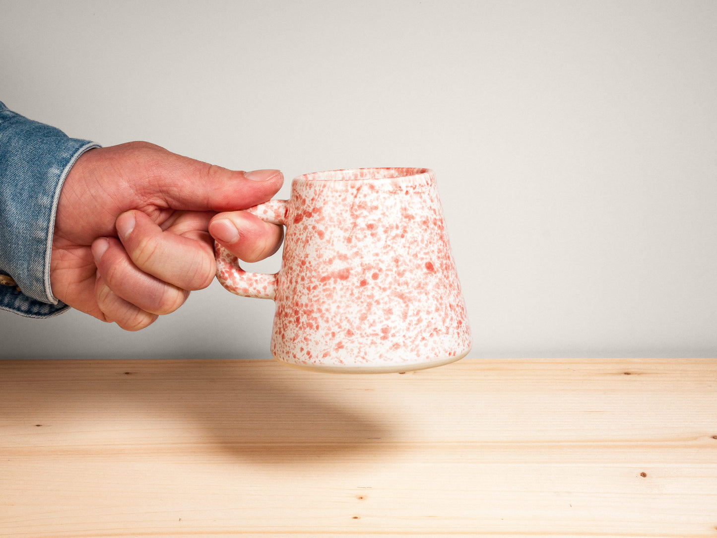 Hand holding a pink and white ceramic mug on wooden surface with plain background