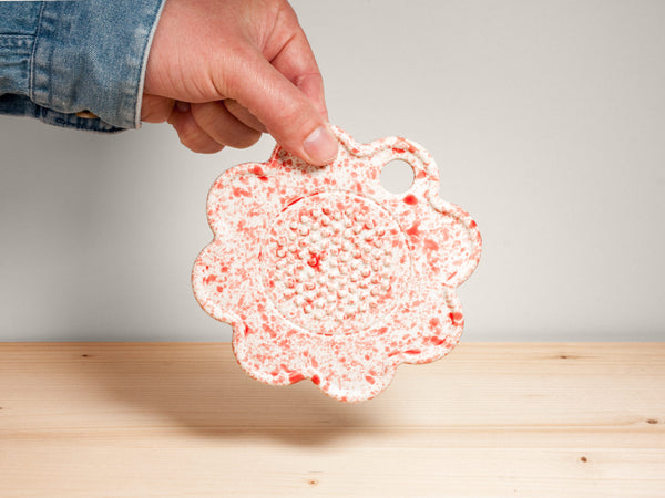 Pink and white flower-shaped ceramic garlic grater on wooden surface