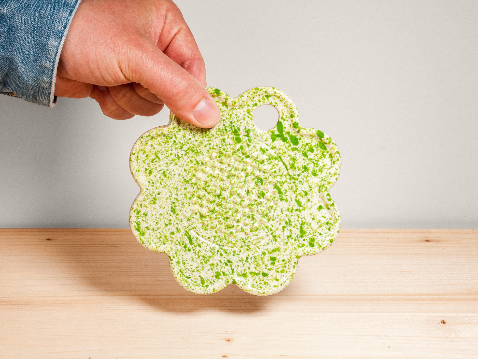 Green and white flower-shaped ceramic garlic grater on wooden surface