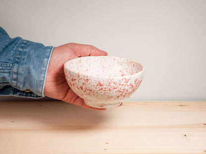 Hand holding a pink and white ceramic bowl on wooden surface