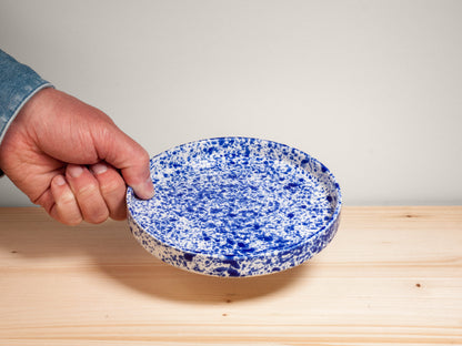 Hand holding a blue and white ceramic plate on wooden surface