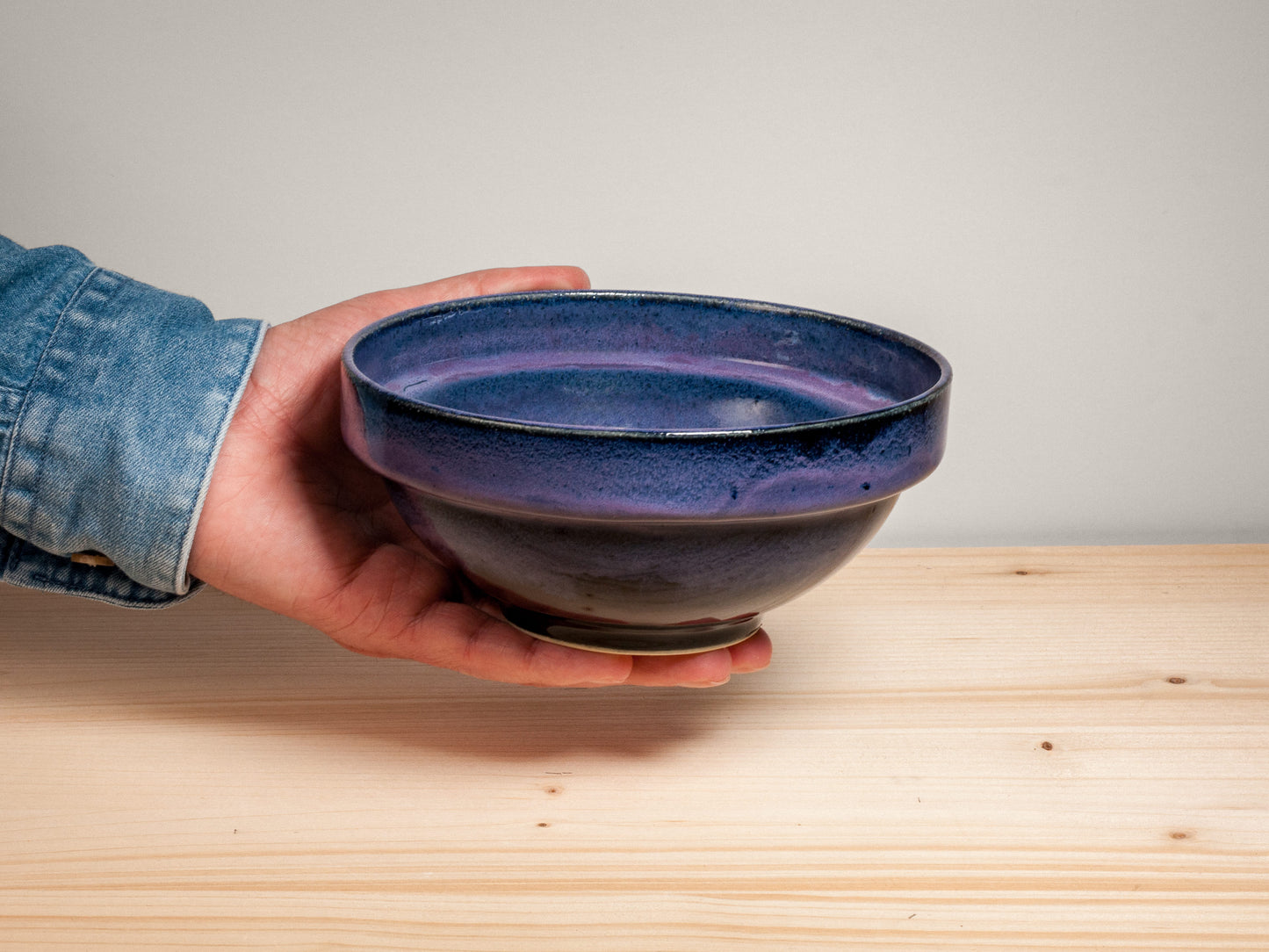 Hand holding a dark purple ceramic bowl on wooden surface