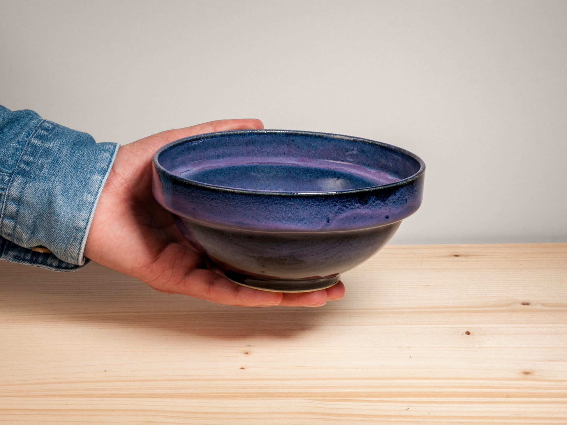 Hand holding a dark purple ceramic bowl on wooden surface