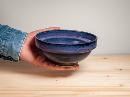 Hand holding a dark purple ceramic bowl on wooden surface