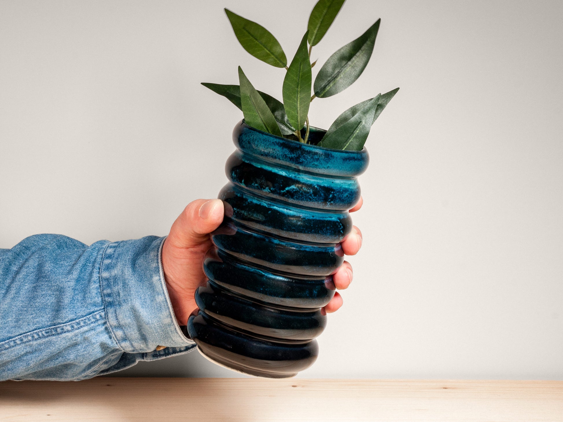 Hand holding a dark teal ceramic vase on wooden surface