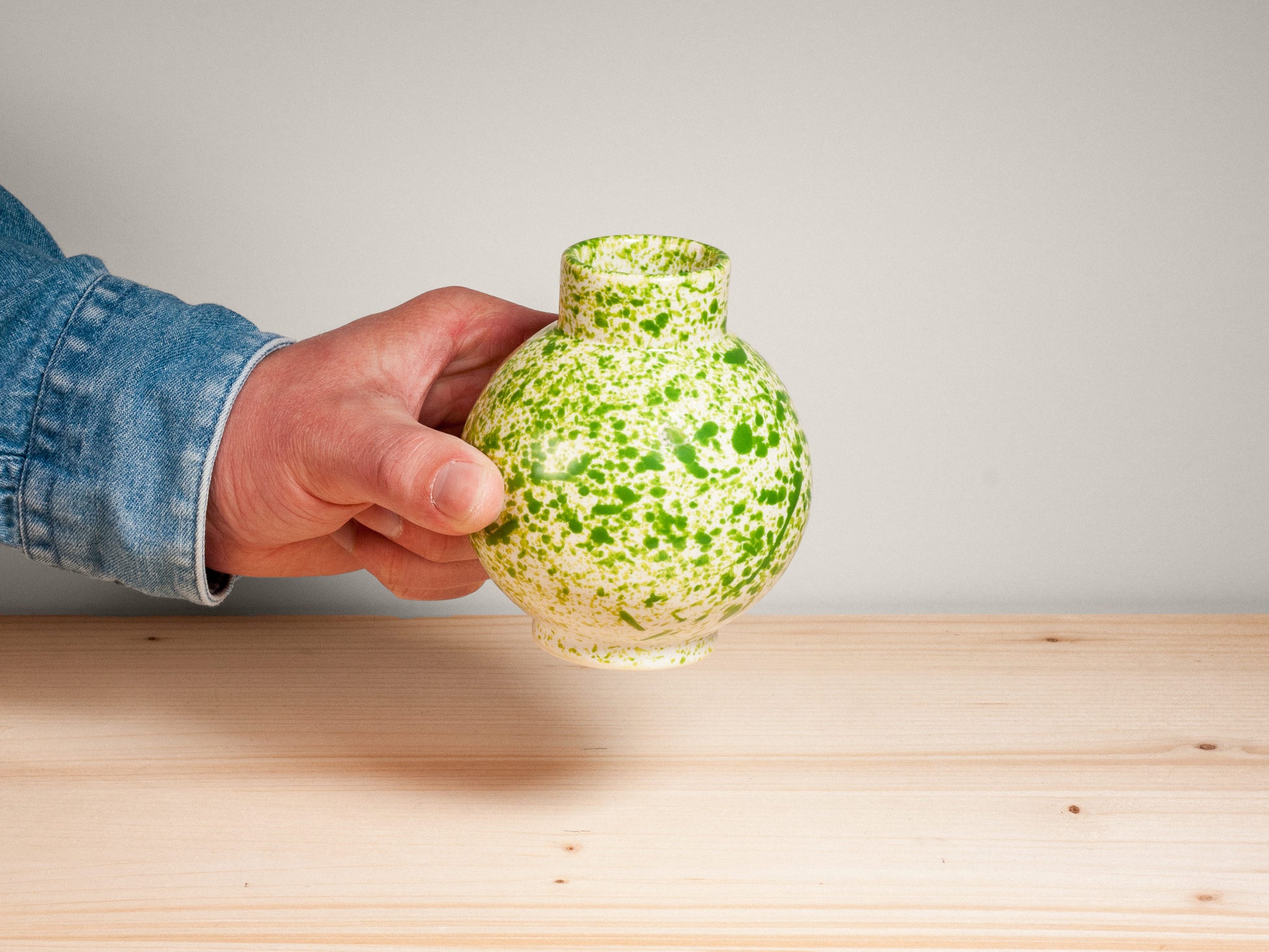 Hand holding green ceramic vase on wooden surface