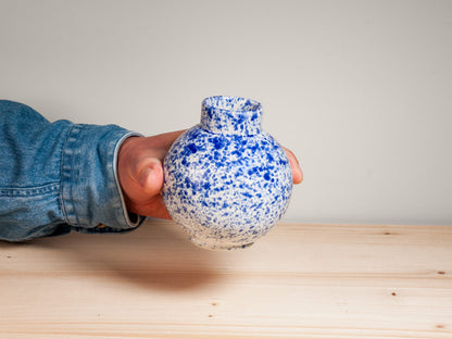 Hand holding a blue and white ceramic vase on wooden surface with plain background