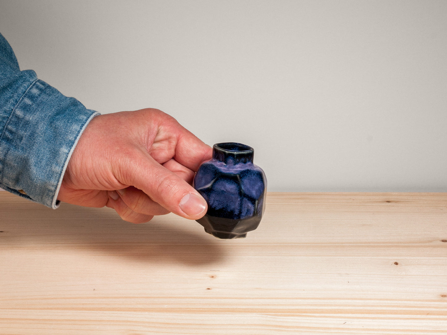 Hand holding a dark purple vase on wooden surface