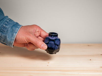Hand holding a dark purple vase on wooden surface