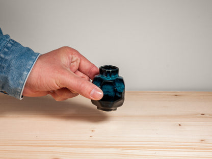 Hand holding dark teal ceramic vase on wooden surface