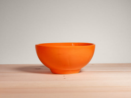 Orange ceramic bowl on a wooden surface with a light gray background