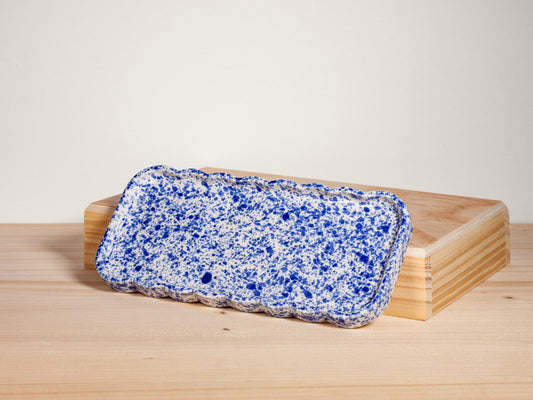 Rectangular blue and white speckled tray on a wooden stand with a light background