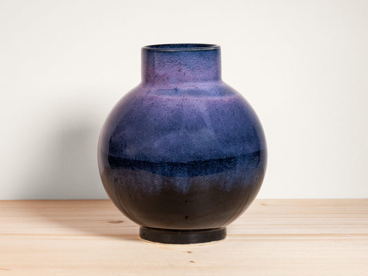 Purple ceramic vase on a wooden surface with a white background