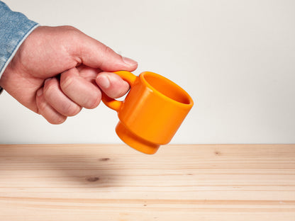 Hand holding an orange mug on a wooden surface with a white background