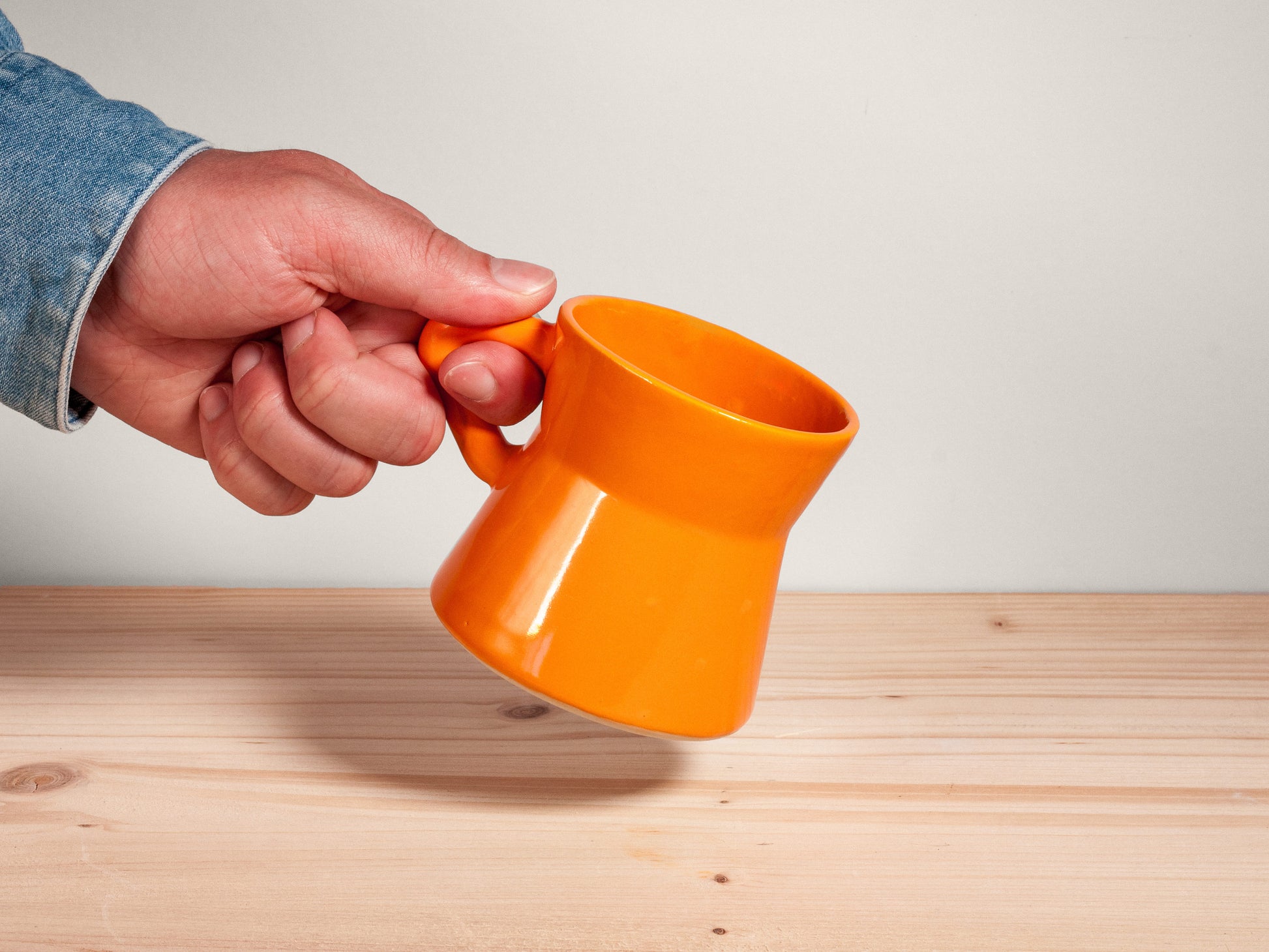 Hand holding an orange ceramic mug on a wooden background
