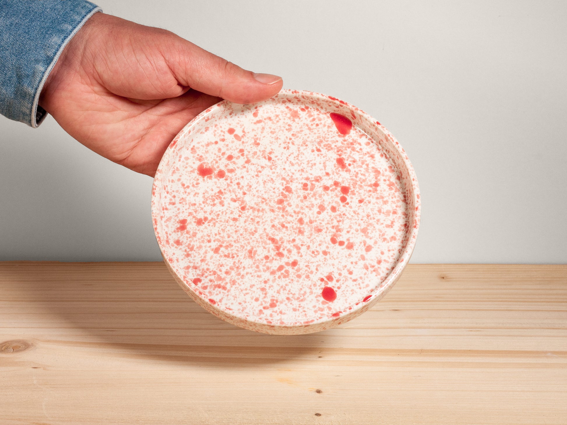 Hand holding a round, speckled plate on a wooden surface with a neutral background