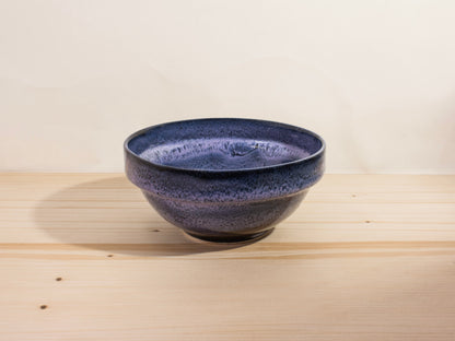 Dark purple ceramic bowl on a wooden surface with a light background