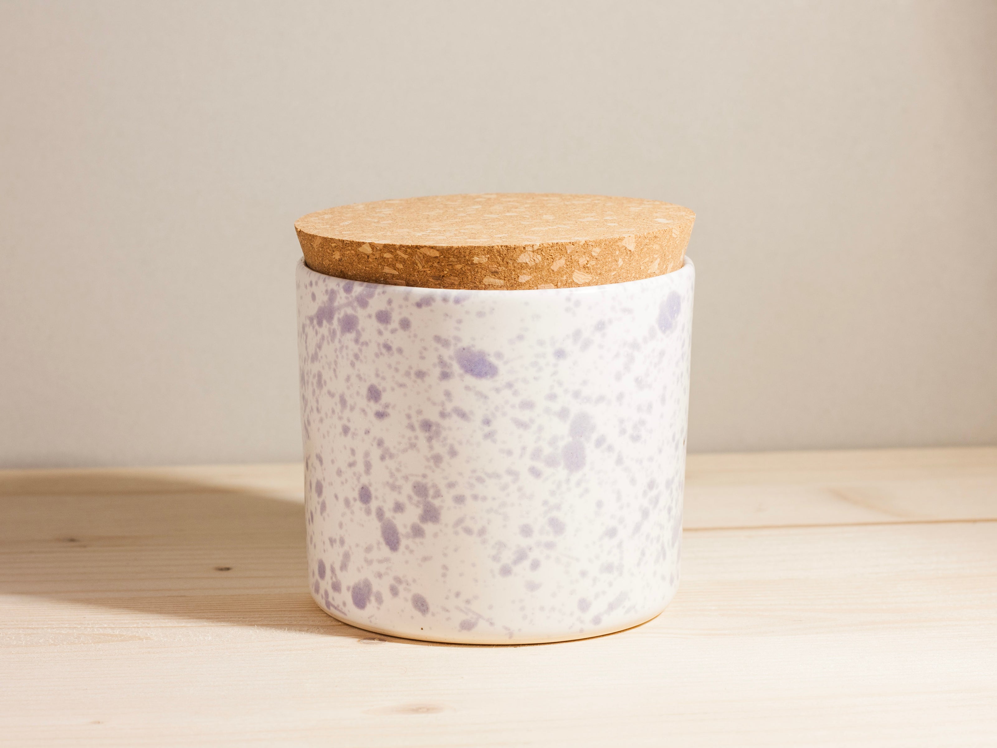 Speckled ceramic jar with cork lid on a wooden surface