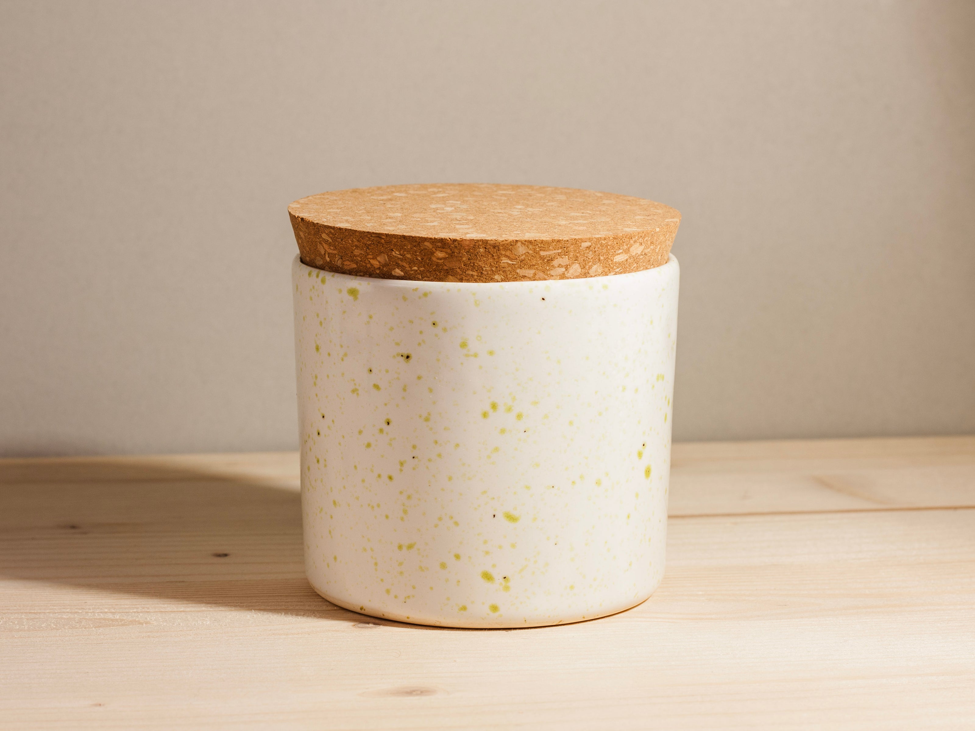 White speckled jar with a cork lid on a wooden surface