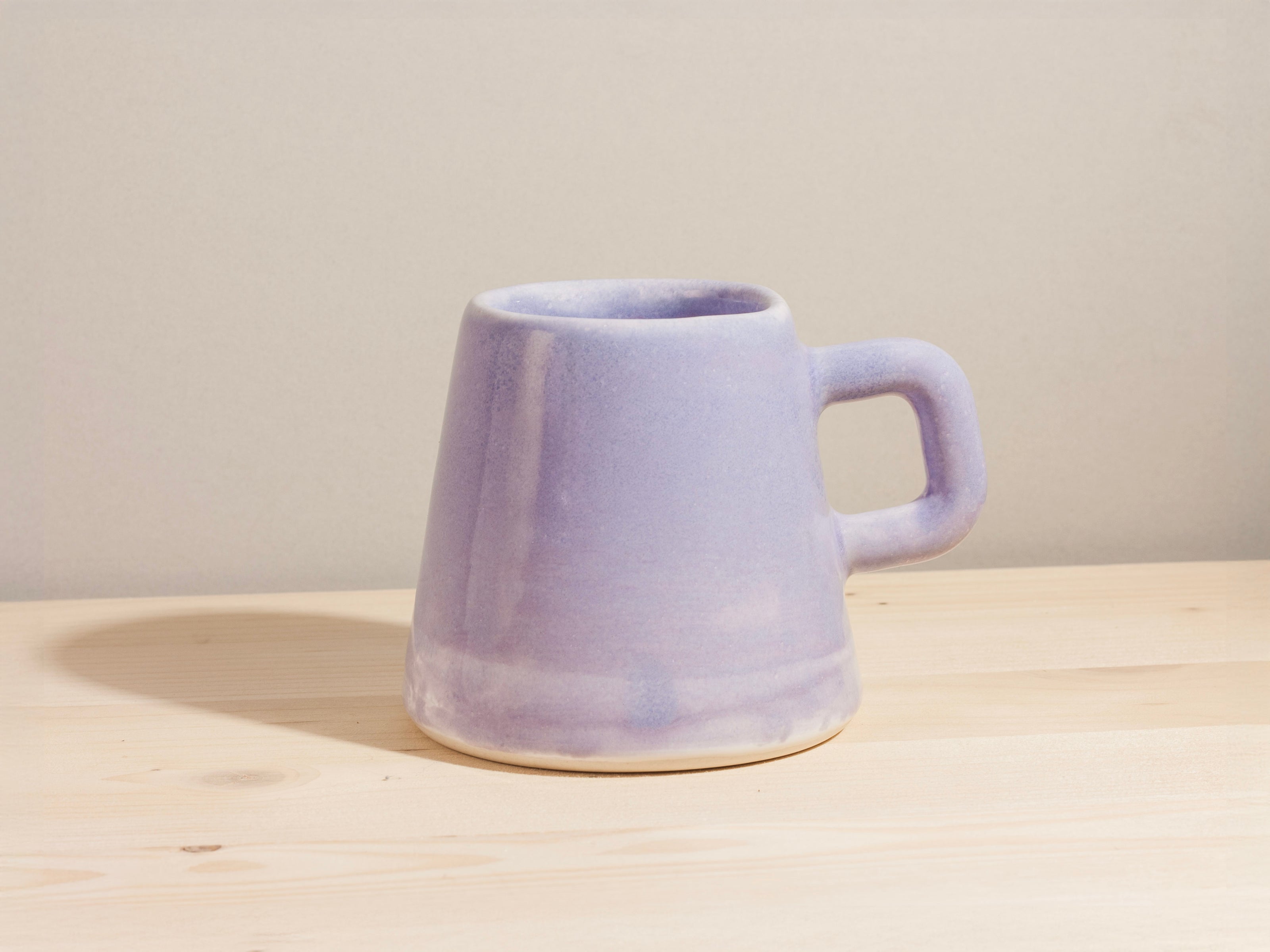 Purple ceramic mug on a wooden surface with a plain background