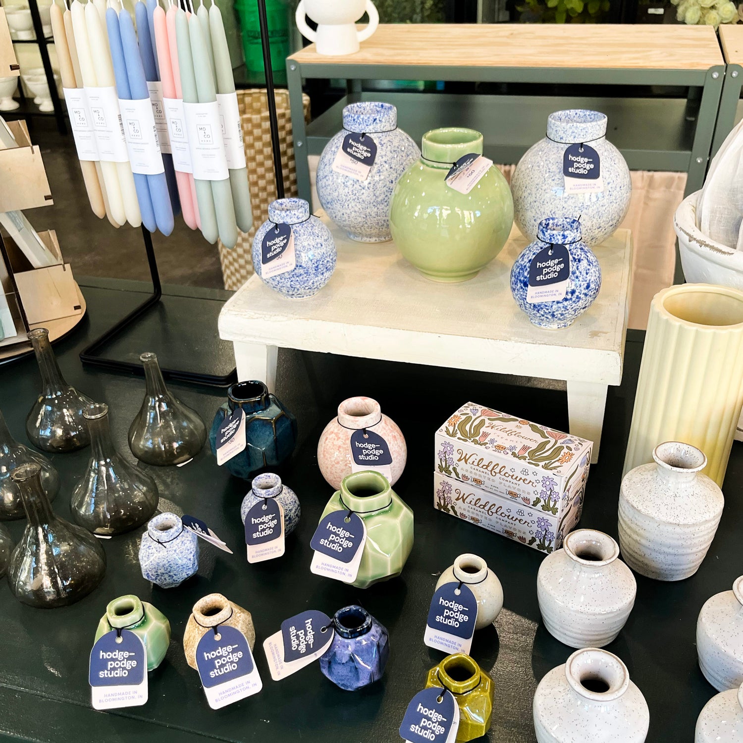 Vases and containers with tags on a display table in a store setting.