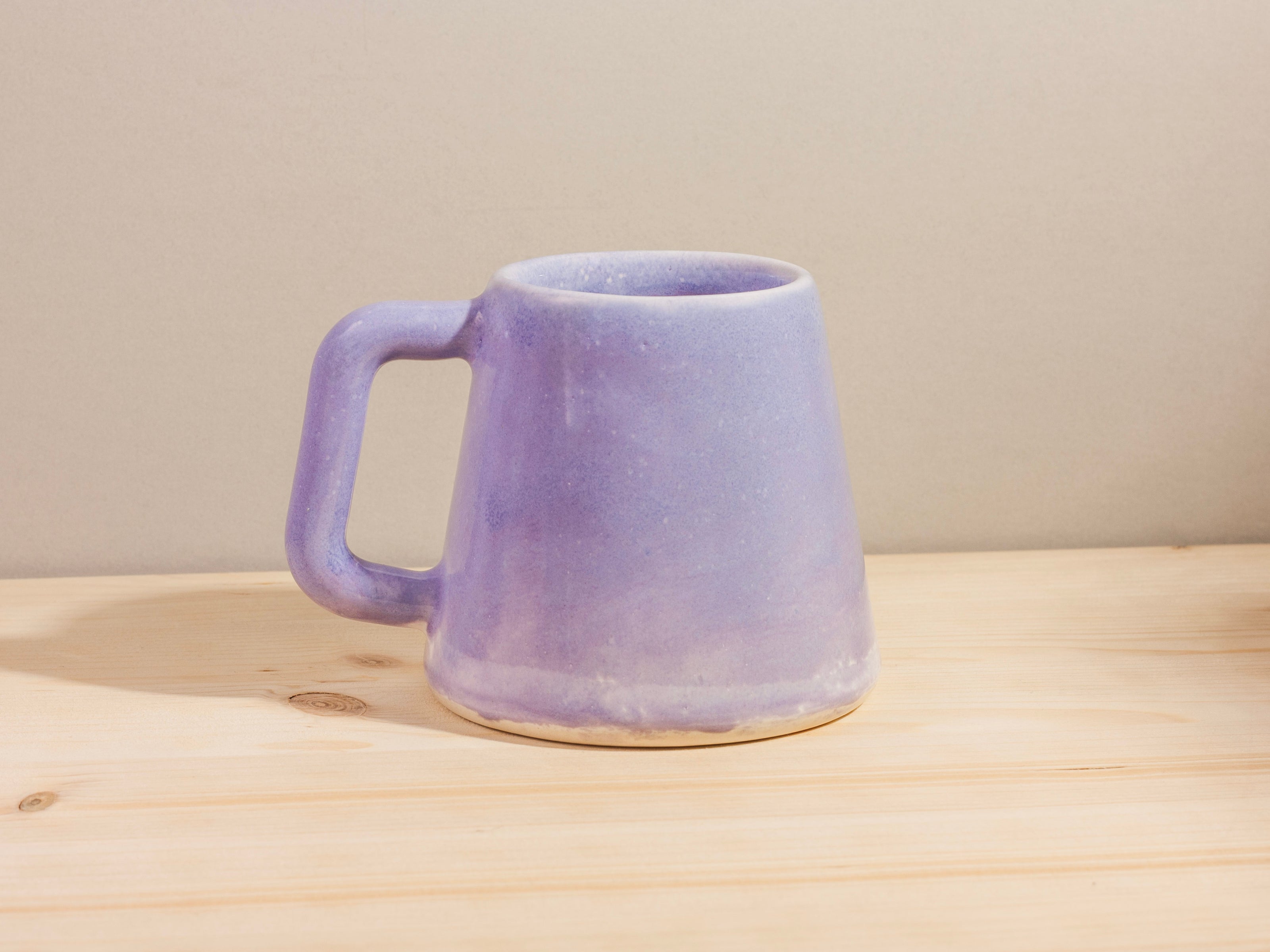 Purple ceramic mug on a wooden surface with a neutral background