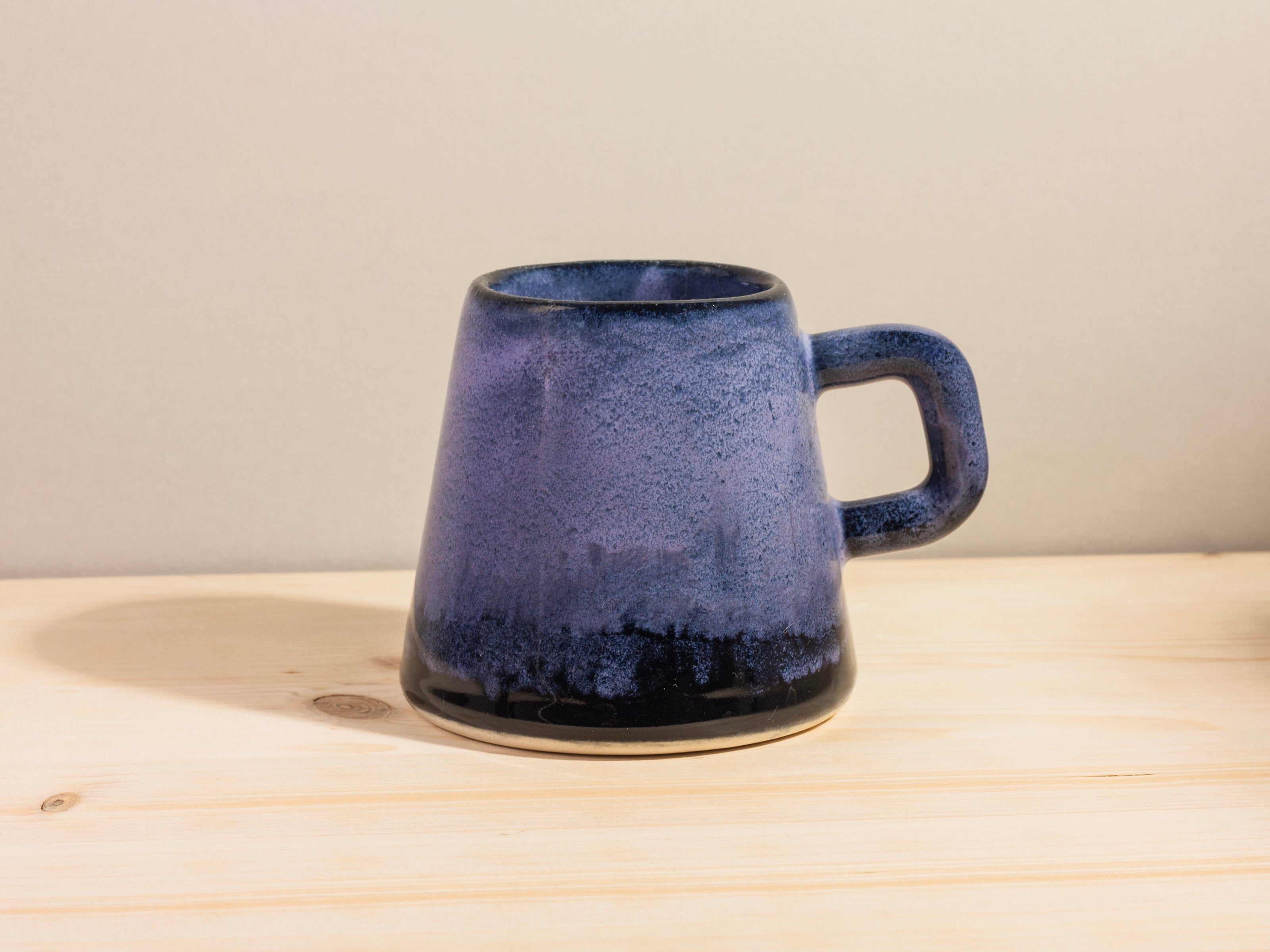 Dark purple ceramic mug on a wooden surface with a beige background