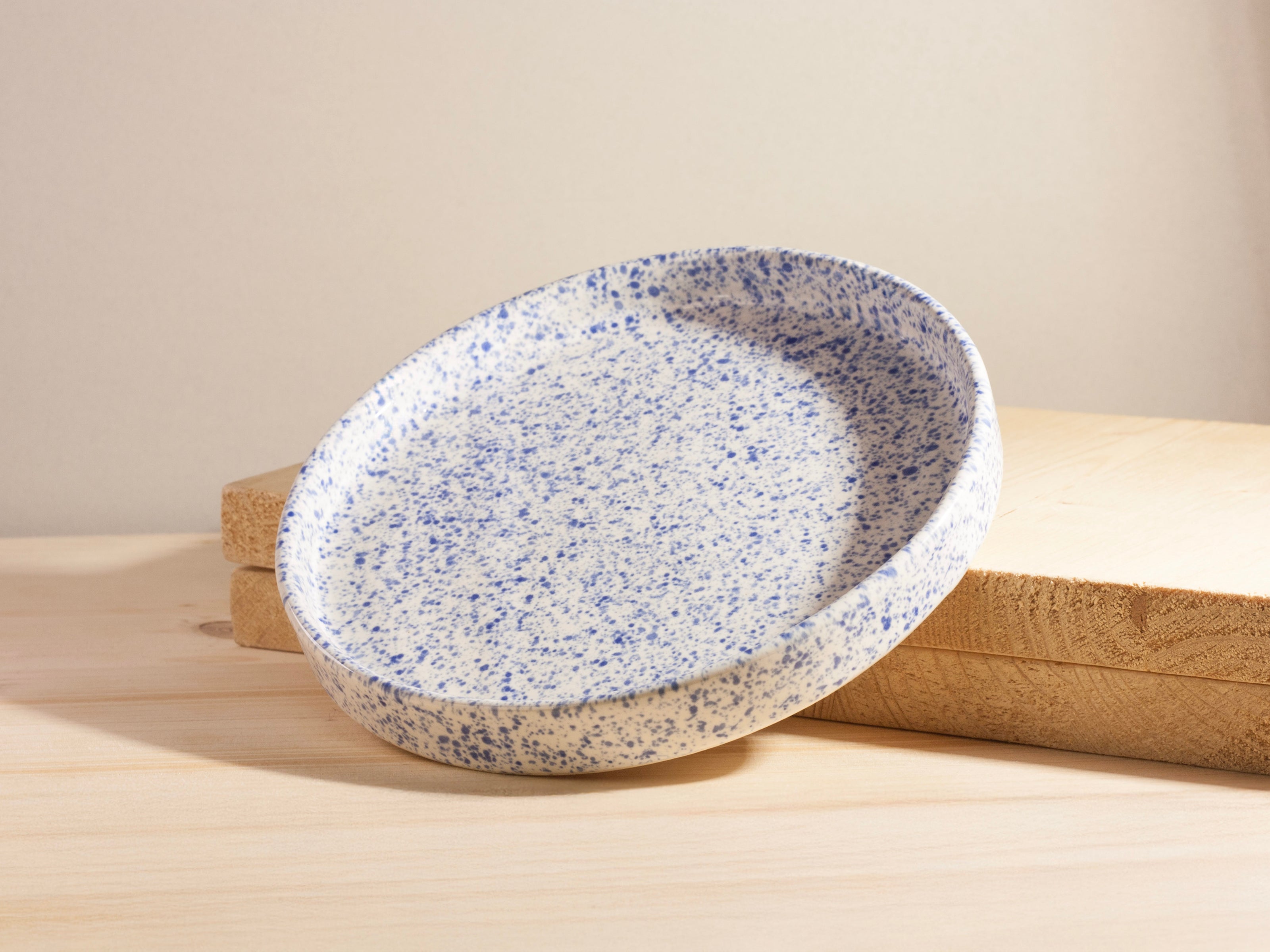 Speckled ceramic bowl on a wooden surface with a beige background